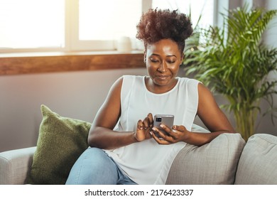 Happy Woman Text Messaging On Smart Phone At Home. Smiling African Woman Daydreaming And Holding Mobile Phone With Copy Space. Happy Beautiful Black Girl Thinking While Using Smart Phone.