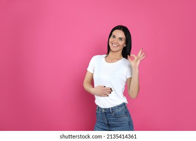Happy woman touching her belly and showing okay gesture on pink background, space for text. Concept of healthy stomach