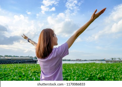 Happy woman tourist standing and raise her hands up on green water plant with blue sky at side of river.