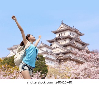 Happy woman traveler enjoy view with sakura cherry blossoms tree and castle on vacation while spring in japan, asian