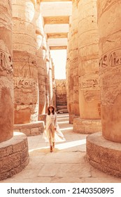 Happy woman traveler explores the ruins of the ancient Karnak temple in the heritage city of Luxor in Egypt. Giant row of columns with carved hieroglyph - Shutterstock ID 2140350895