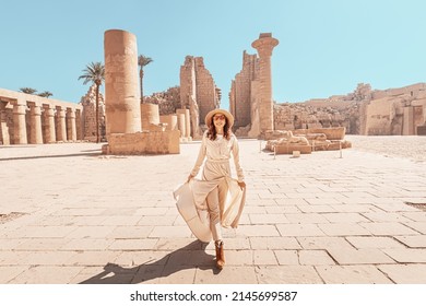 Happy woman traveler explores the ruins of the ancient Karnak temple in the heritage city of Luxor in Egypt. Giant row of columns with carved hieroglyph - Shutterstock ID 2145699587