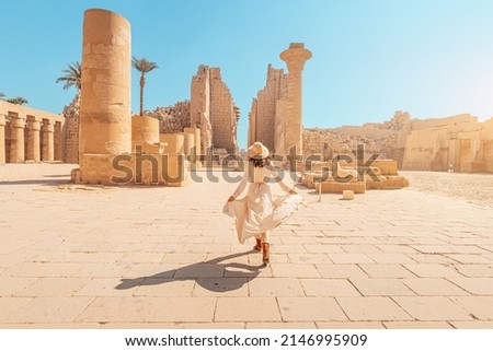 Happy woman traveler explores the ruins of the ancient Karnak temple in the heritage city of Luxor in Egypt. Giant row of columns with carved hieroglyph