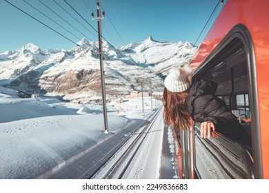 Happy woman traveler looks out from window traveling by train in beautiful winter mountains, Travel concept.