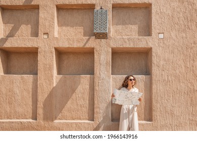 Happy woman travels alone and looks at a map against the wall of an ancient city in the Middle East region or somewhere in Morocco.