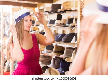 Happy Woman Try On Lady's Hat And Looking In Mirror At Outlet Store