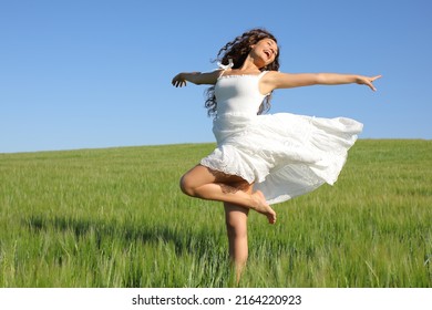 Happy woman twirling with white dress and perfect legs in a green wheat field