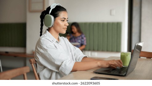 Happy woman, typing and laptop with headphones at cafe for remote work, email or copywriting. Female person, customer or freelancer on computer for writing, journalism or communication at coffee shop
