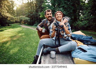 Happy woman using binoculars and exploring the nature with her boyfriend while relaxing on their camper trailer in the woods. Copy space.  - Powered by Shutterstock