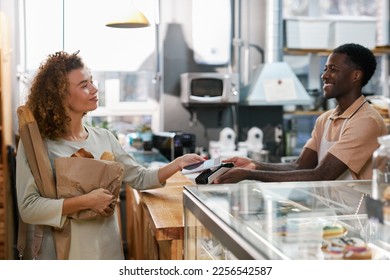 Happy woman using contactless payment app when paying for bread in local bakery - Powered by Shutterstock