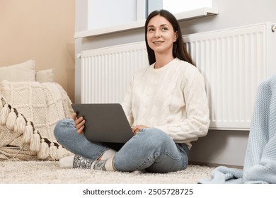 Happy woman using laptop near heating radiator at home