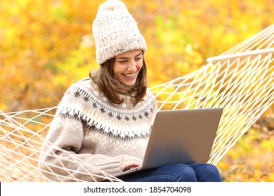 Happy woman using laptop sitting on hammock in fall season in a forest - Powered by Shutterstock