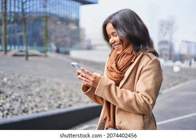 Happy woman using mobile phone outdoors in the city during fall wearing coat