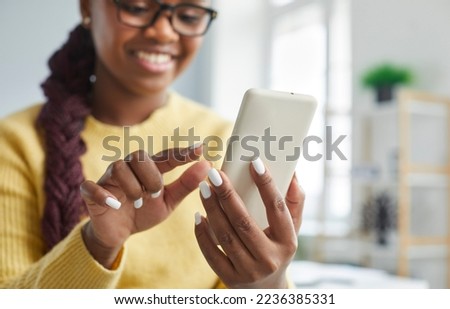 Happy woman using mobile phone. Young African American woman sitting at home, holding cell phone, reading chat, sending text messages and smiling. Closeup shot. Technology concept