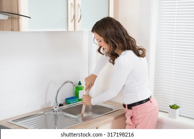 Happy Woman Using Plunger In Kitchen Sink At Home