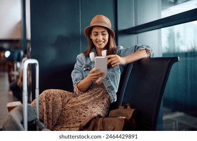 Happy woman using smart phone while waiting for her flight at departure area. Copy space.  - Powered by Shutterstock