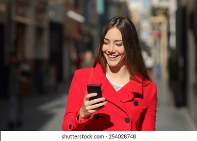 Happy woman using a smart phone while is walking in the street in a sunny day