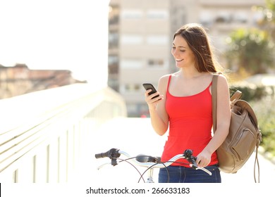 Happy woman using a smart phone walking with a bicycle in an urban park - Powered by Shutterstock