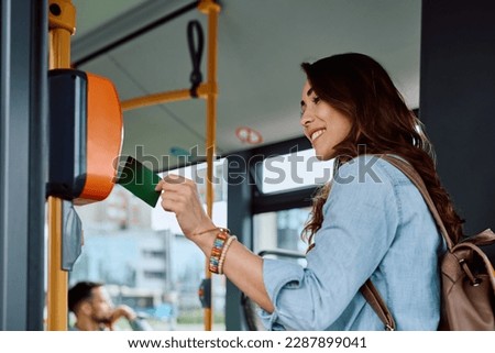 Happy woman using validating card while onboarding in a bus,