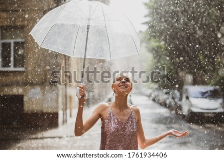 Happy woman walking under summer rain. Outdoor portrait of young beautiful smiling lady holding transparent umbrella, posing in street of European city. Copy, empty space for text