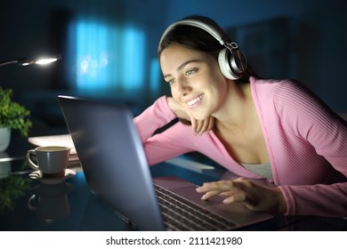 Happy woman watching media with laptop and headphones in the night at home