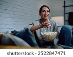 Happy woman watching movie and eating popcorn while relaxing in the evening at home. 