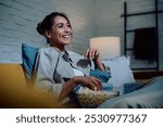 Happy woman watching movie and eating popcorn at night at home.