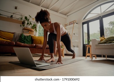 Happy woman watching video on laptop while exercising on yoga mat at home - lock down workout