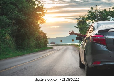 Mujer feliz saludando con la mano afuera del auto de la ventana abierta con pradera y fondo de montaña. Estilo de vida femenino relajante como viajera en viaje por carretera en vacaciones de vacaciones. Transporte y viajes.