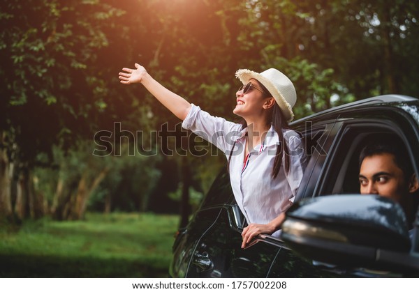 Happy woman waving hand outside open window car\
with her boyfriend on forest background. People lifestyle relaxing\
as traveler on road trip in holiday vacation. Transportation and\
weekend travel