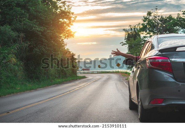 Happy woman\
waving hand outside open window car with meadow and mountain\
background. Female lifestyle relaxing as traveler on road trip in\
holiday vacation. Transportation and\
travel.