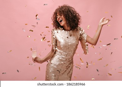 Happy woman with wavy dark hair style in shiny trendy clothes rejoicing, holding glass with champagne and posing with confetti on pink backdrop.. - Powered by Shutterstock