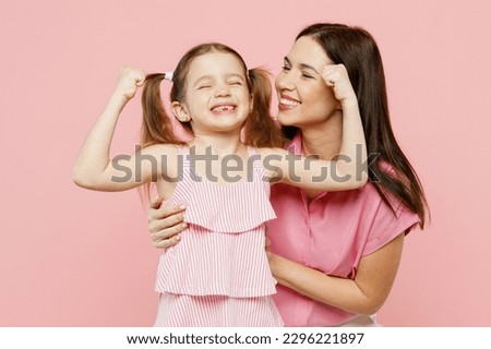 Happy woman wearing casual clothes with child kid girl 6-7 years old. Mother daughter show hand biceps muscles demonstrate strength isolated on plain pastel pink background. Family parent day concept