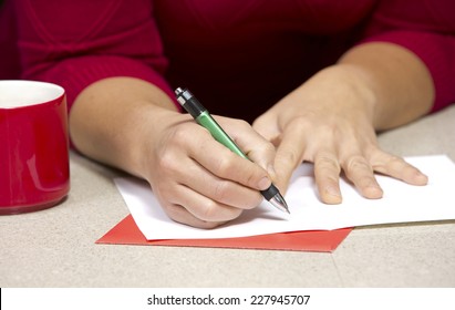 Happy Woman Wearing Christmas Hat In The Kitchen Writing A Card