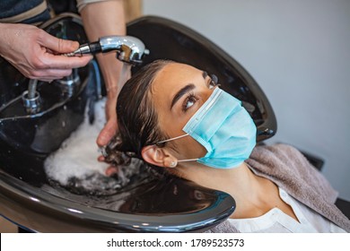 Happy woman wearing face mask while hairdresser is washing her hair at the salon during COVID-19 epidemic. Young woman with surgical mask on face at hairdresser salon. Covid-19 concept. - Shutterstock ID 1789523573
