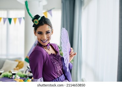 Happy Woman Wearing Mardi Gras Make-up And Costume At Home And Looking At Camera.