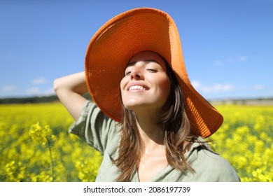 Happy woman wearing orange pamela smiling in a yellow flowered field
