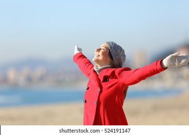 Happy woman wearing a red jacket breathing fresh air and raising arms on the beach in a sunny day of winter - Powered by Shutterstock