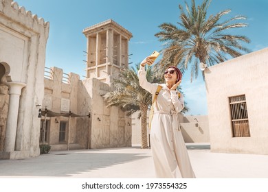 Happy woman wearing a turban hat takes a selfie photo on her smartphone against the background of a Bur Dubai old town near Creek district - Powered by Shutterstock