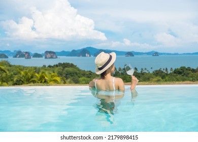 Happy Woman In White Swimsuit Drinking Wine In Luxury Swimming Pool Hotel Against Beautiful View, Young Female With Hat Enjoy In Tropical Resort. Relaxing, Summer Travel, Holiday And Vacation Concept