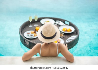 Happy Woman In White Swimsuit Having Floating Breakfast Tray In Luxury Pool Hotel, Young Female With Hat Enjoy In Tropical Resort. Relaxing, Exotic Summer Travel, Holiday, Vacation And Weekend