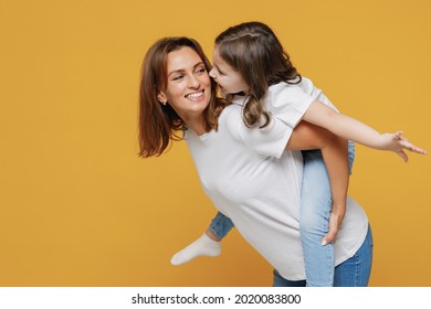 Happy woman in white t-shirt have fun with cute child baby girl 5-6 years old sit on back. Mommy little kid daughter isolated on yellow orange color background studio. Mother's Day love family concept