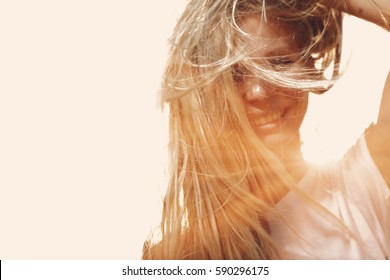 Happy woman with windy messy hair backlit by sun selective focus colorized image, copy space. Jolly girl windswept hair full of sunshine glow.