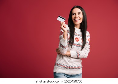 Happy Woman In Winter Sweater Holding Credit Card, Isolated On Red 