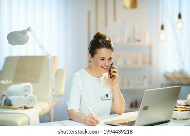 happy woman worker with laptop speaking on a smartphone in modern beauty salon.