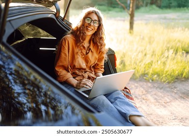 Happy woman working with laptop from the car trunk or boot in camper sunny summer park. Digital nomad freedom lifestyle concept, travel freelancer and vacations. - Powered by Shutterstock