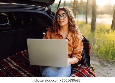 Happy woman working with laptop from the car trunk or boot in camper sunny summer park. Digital nomad freedom lifestyle concept, travel freelancer and vacations. - Powered by Shutterstock