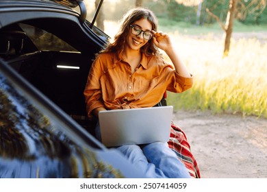 Happy woman working with laptop from the car trunk or boot in camper sunny summer park. Digital nomad freedom lifestyle concept, travel freelancer and vacations. - Powered by Shutterstock