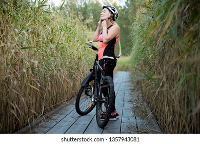 Happy woman working out, leisure activity, putting on helmet. Girl traveling by bike on wooden trail in field of reeds - Powered by Shutterstock