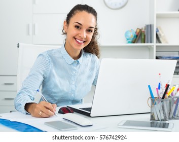 Happy woman working with paperwork and laptop in office